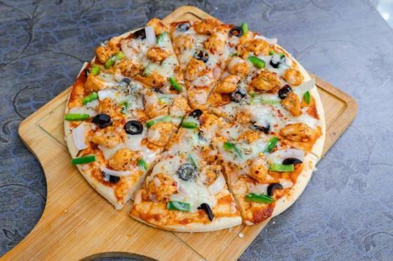 Homemade chicken pizza with olives and capsicum on a wooden board